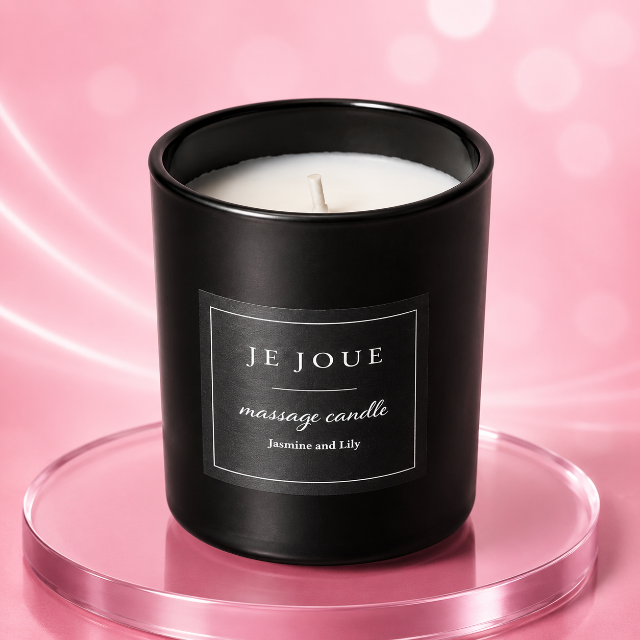 Schwarze Massagekerze mit weißem Wachs, Label mit Aufschrift JE JOUE massage candle Jasmine and Lily, auf rosafarbenem Untergrund
